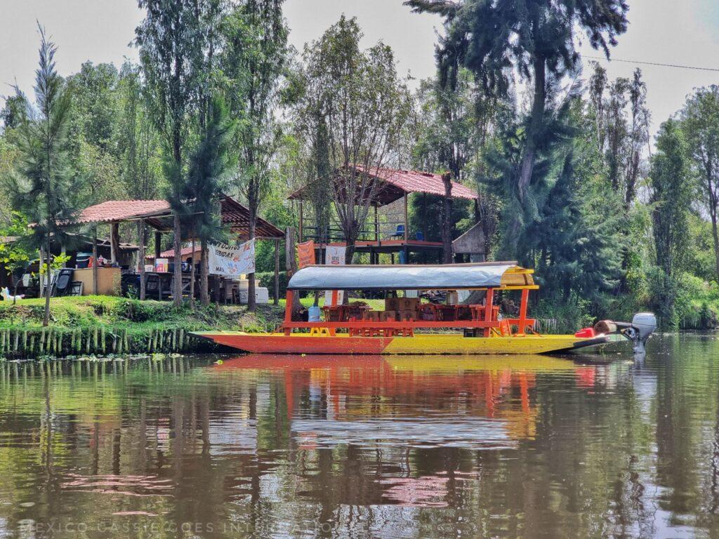 red and yellow boat on calm water, reflection is clear, green trees 