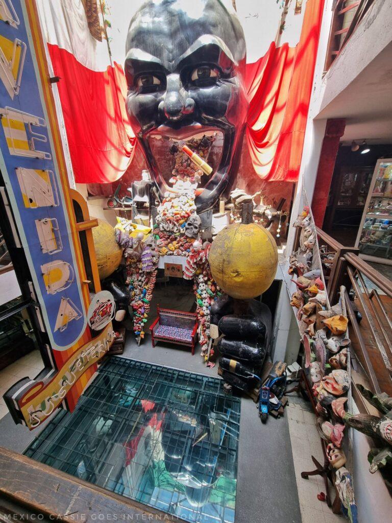 very odd display with large face with open mouth, toys spilling out of mouth. Mexican flag draped around it