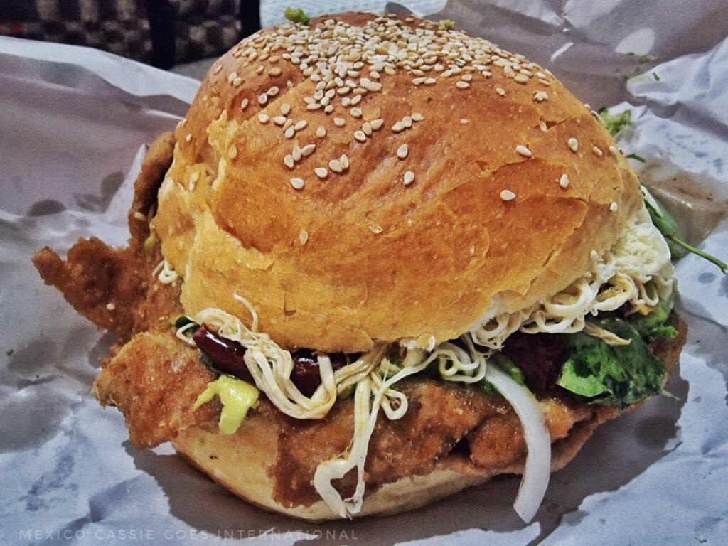 full cemita (bread roll with sesame seeds on top - you can see breaded pork, cheese, chile and lettuce sticking out
