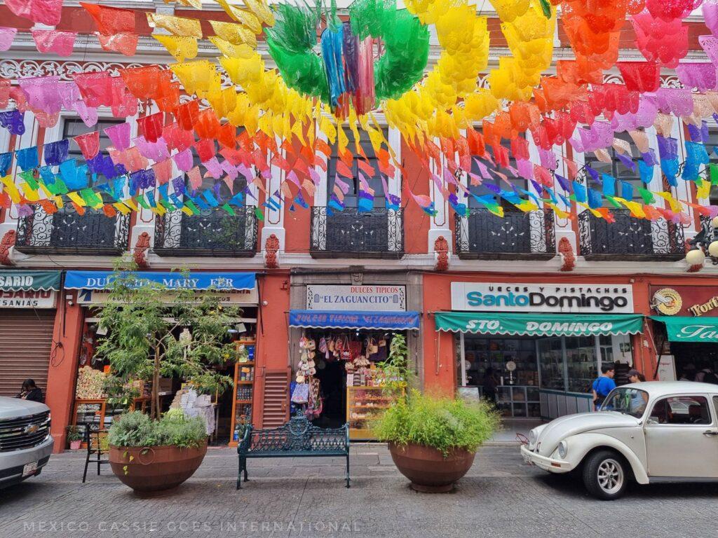regular Mexican street scene, white VW beetle to one side and colourful rainbow bunting circling out over the street