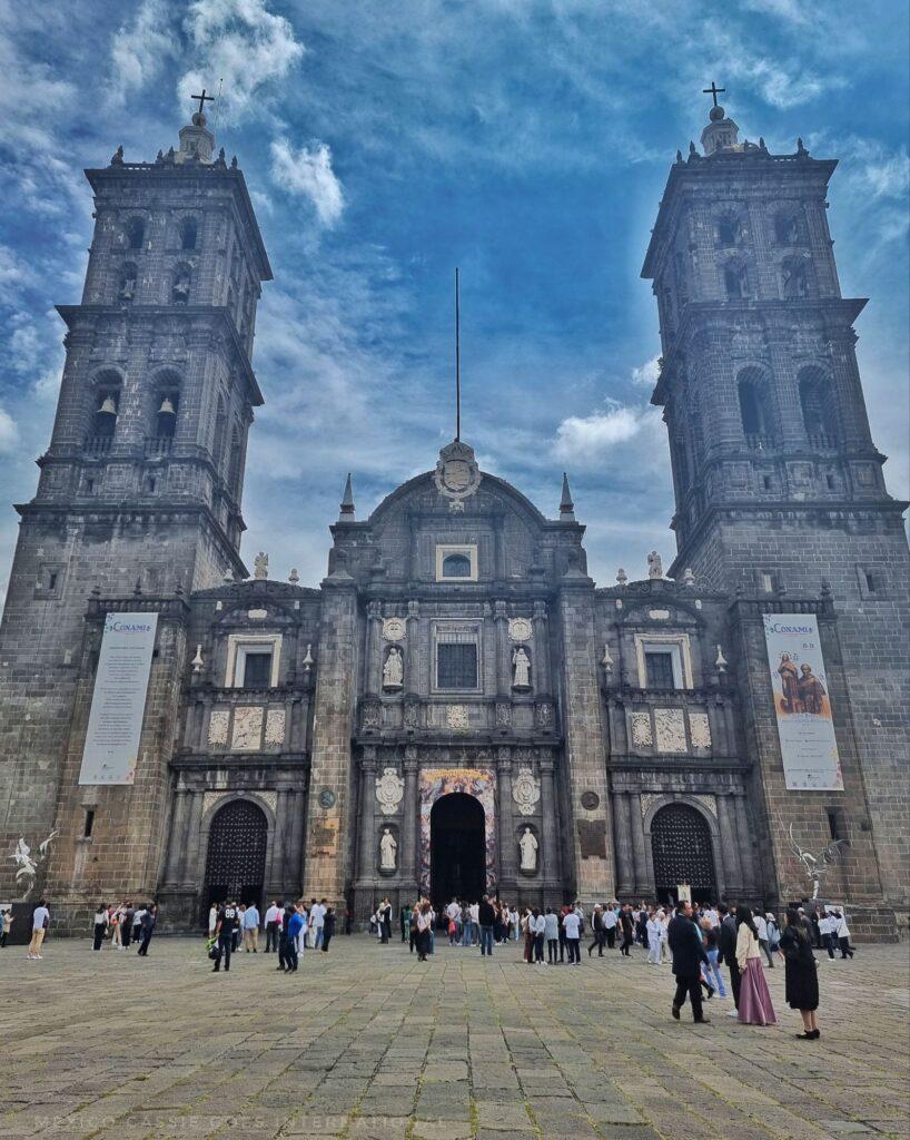 front view of cathedral with 2 towers, people milling around
