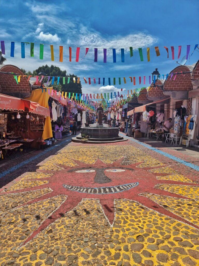 market street, floor is cobbles painted with red sun and yellow all around. sun has a face, colourful bunting over the street