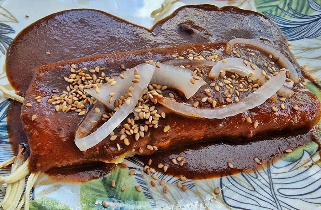 tamal with mole poblano sauce (brown), slices of white onion and sesame seeds on it