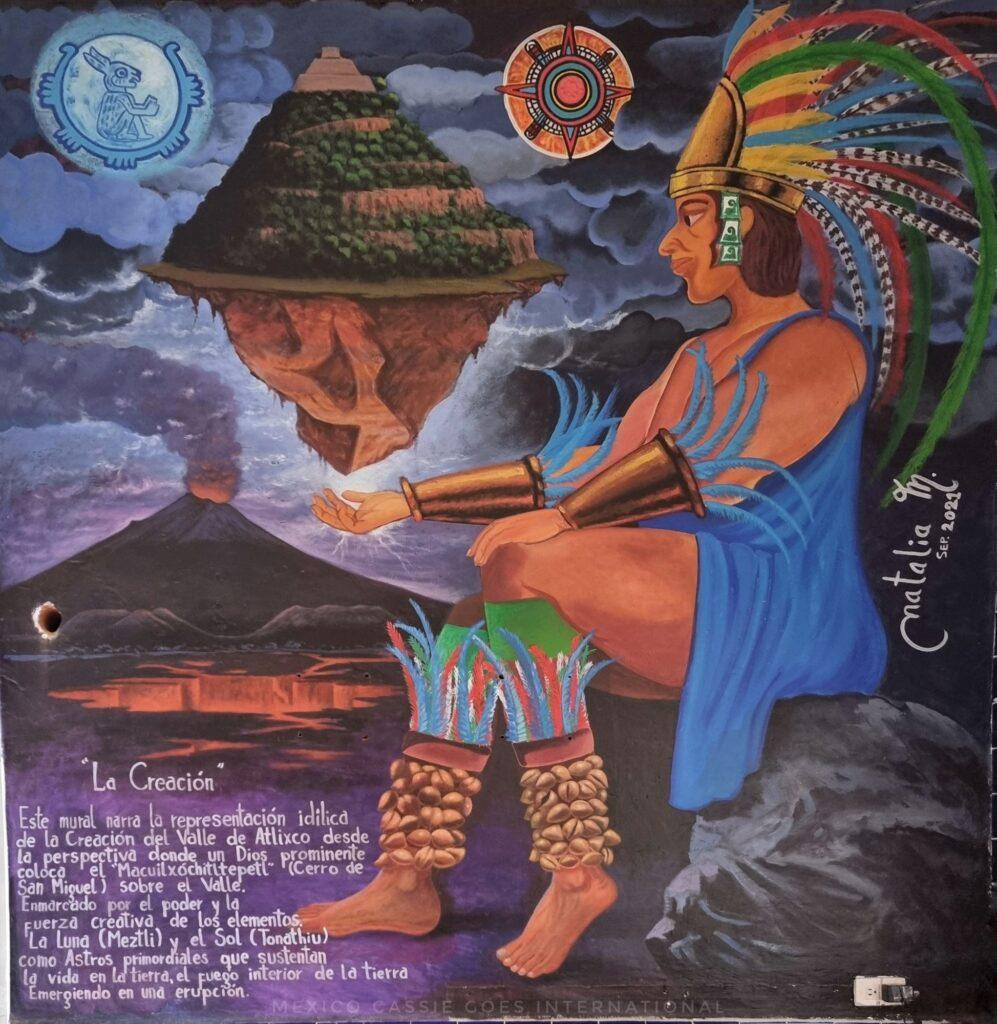 mural of a god at creation - in headdress, land is balancing in his hand. volcano in background. text about creation in bottom left (spanish)