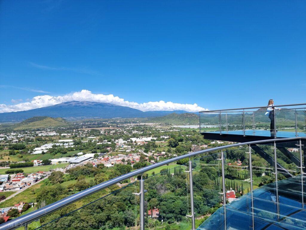 glass walk way over fields, volcano over to left