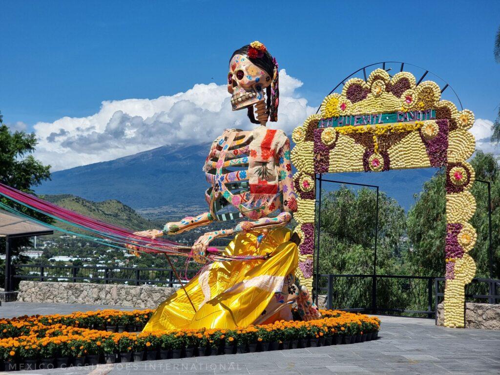 giant skeleton in yellow skirt weaving - Popocatéptl in background