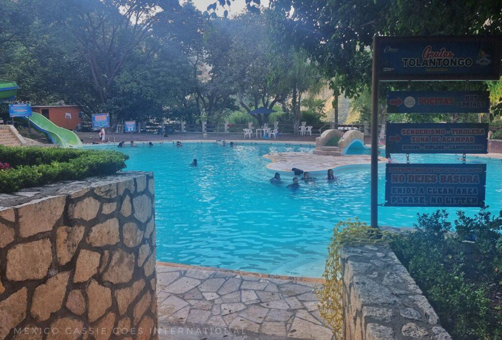 open air swimming pool (photo taken from end of the path to the pool, island in middle, can just see the water slide on left. signs blocking view on right