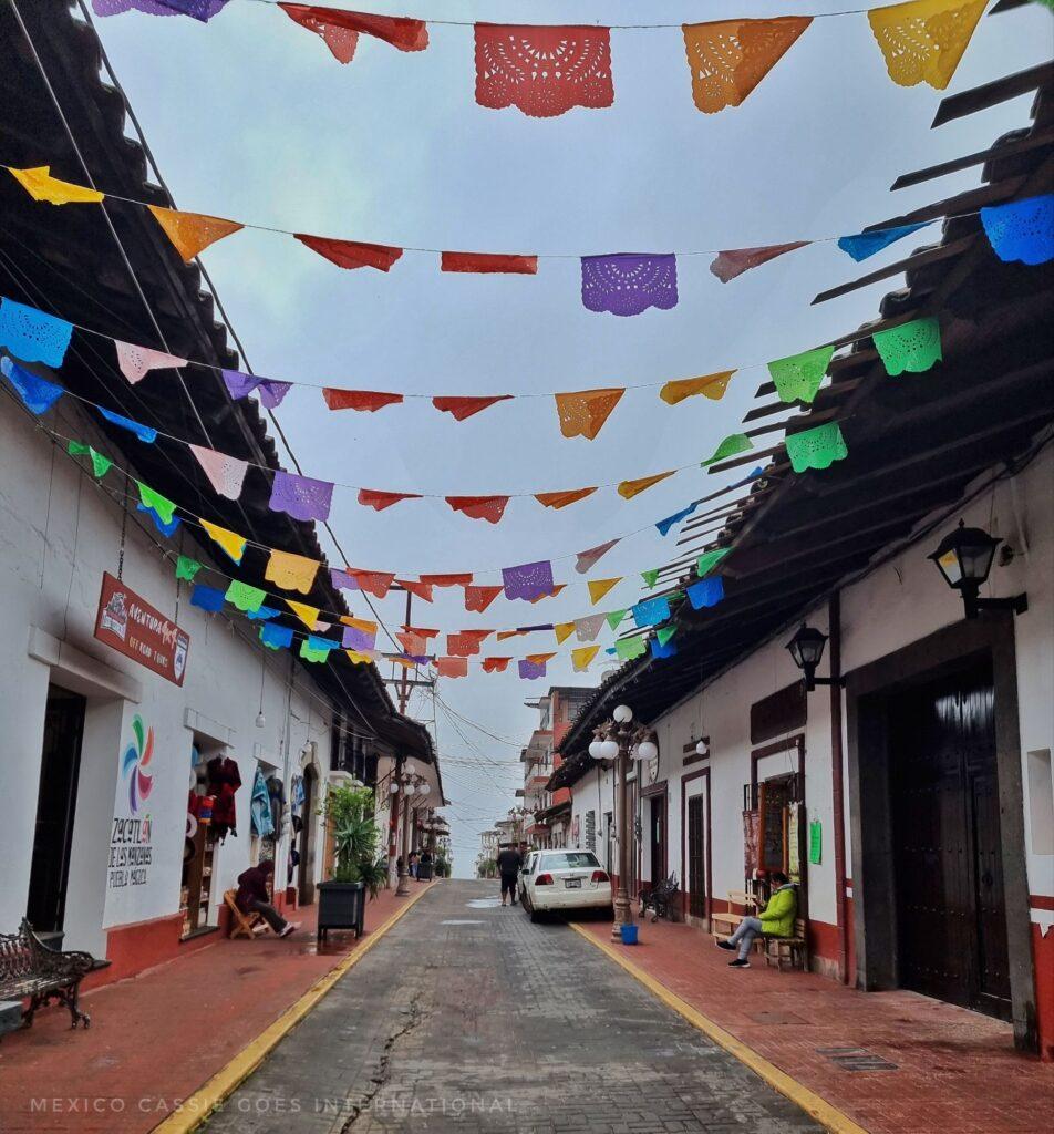 street scene, red pavements, white buildings with heavy roofs, mexican papel picado strung across road