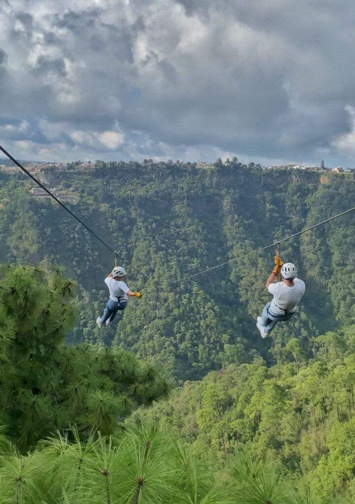 2 people ziplining over a canyon that's covered in trees