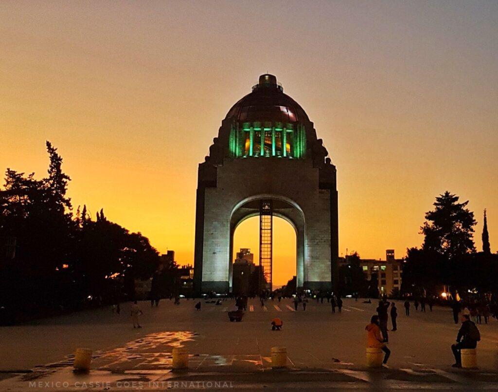 monumento a la revolucion at night, orange sky lit up behind the impressive monument