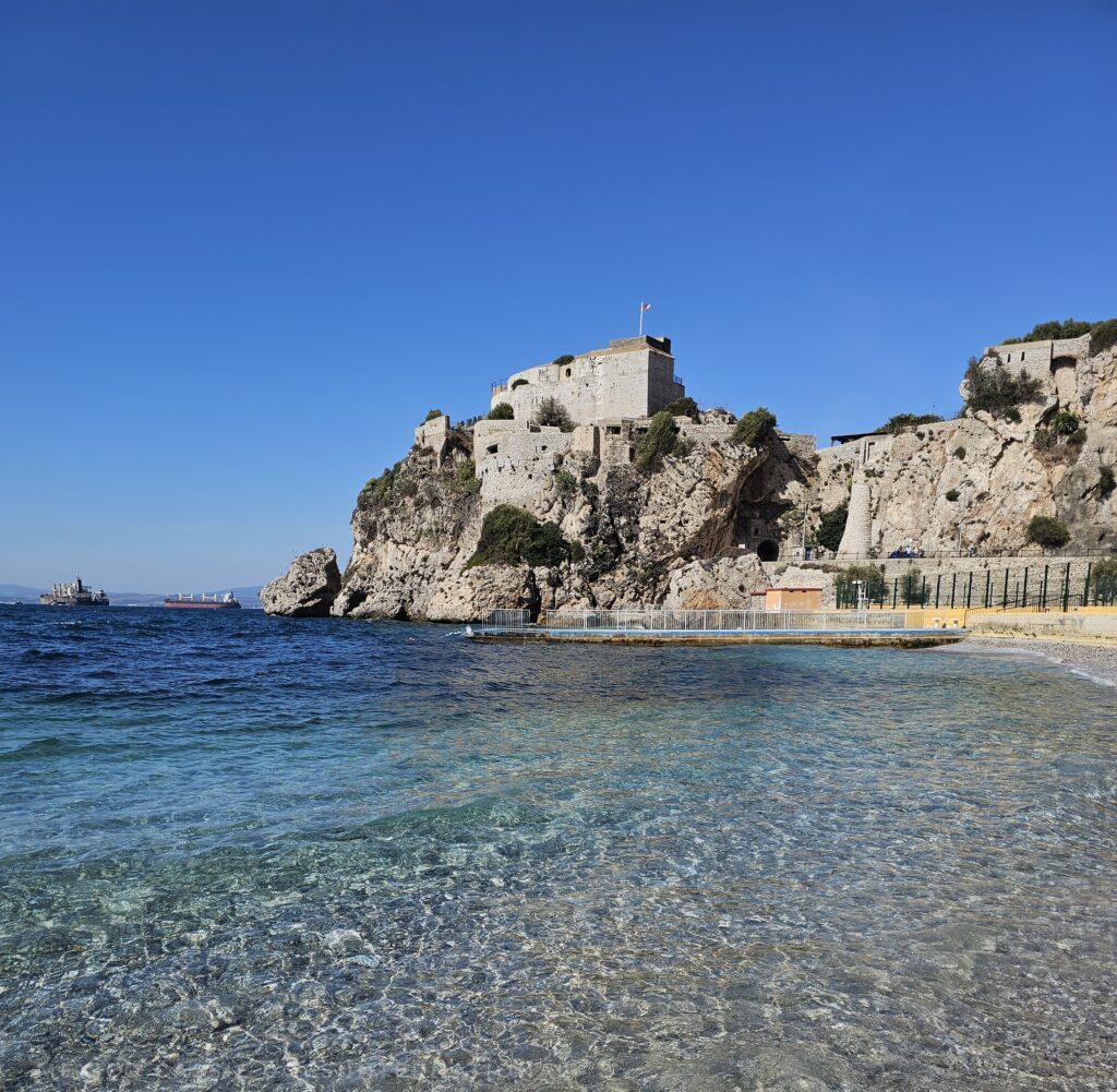 stoney beach with perfect clear water, buildings on cliff in distance