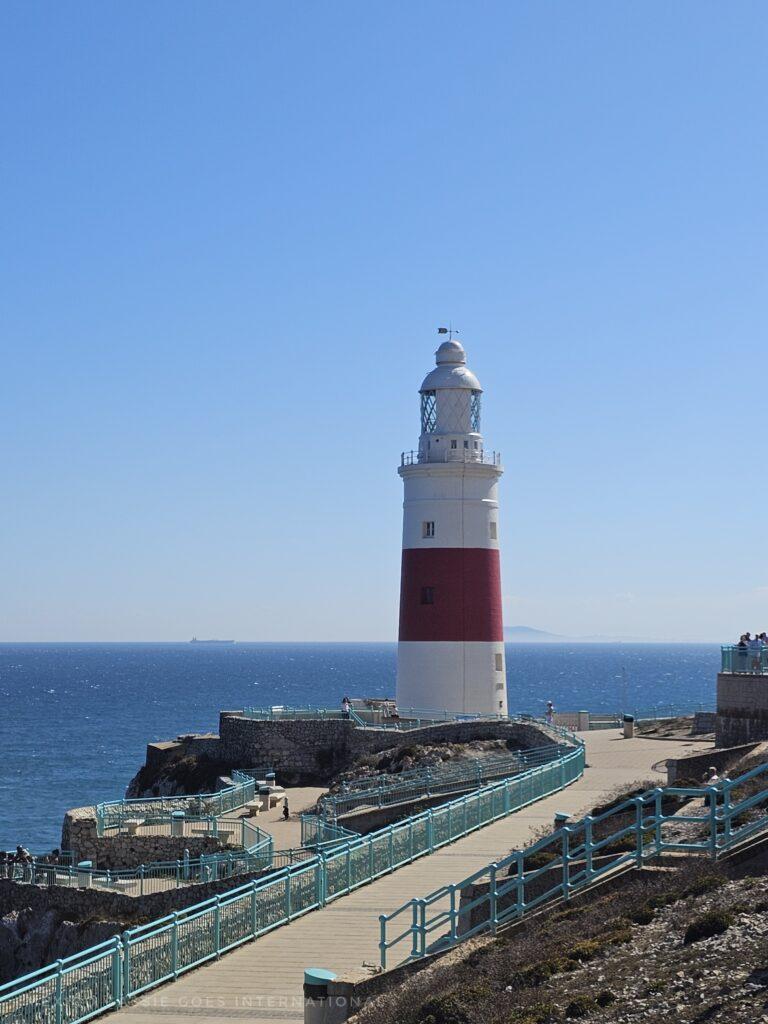 small red and white lighthouse on bright sunny day, Morocco visible behind, path in front to lighthouse