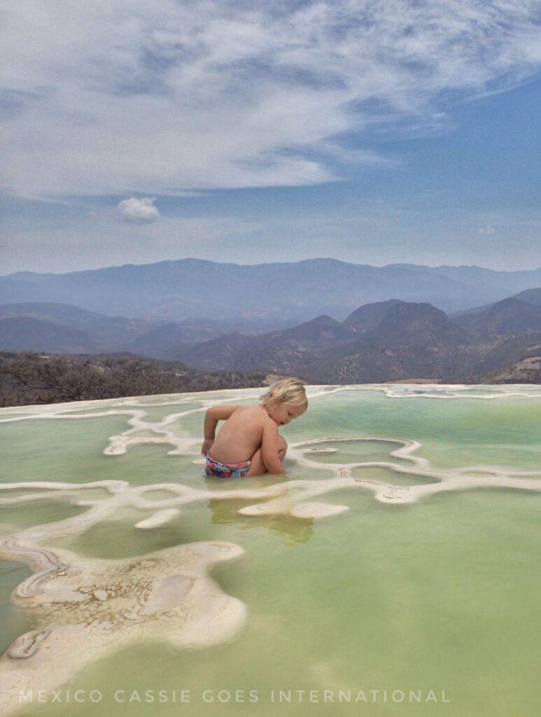 small child playing in greenish water, mountain views in background