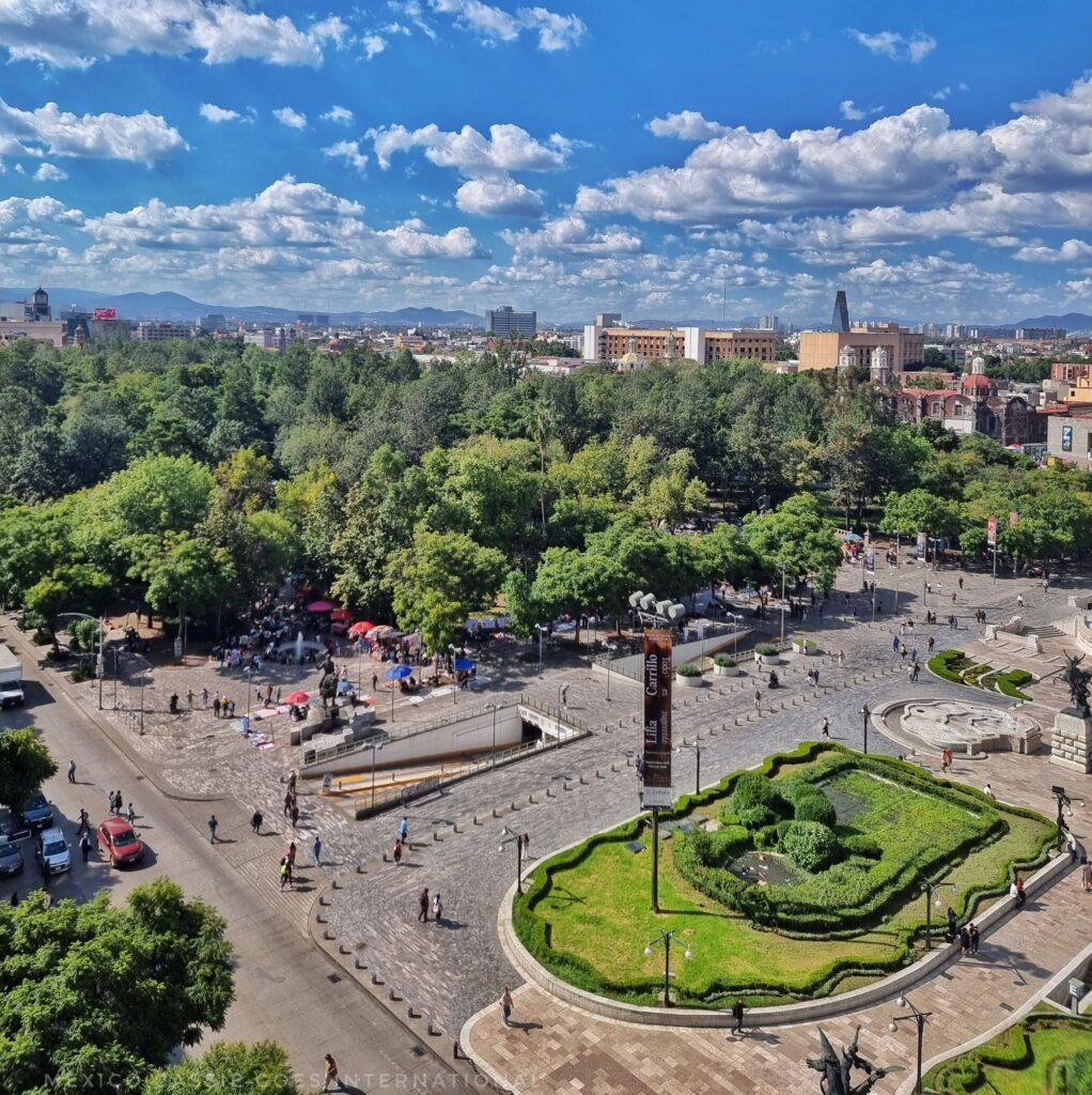 aerial view of the alameda - full of trees, some grassy spaces, large pedestrian zone. mountains just visible in the back, blue cloudy sky