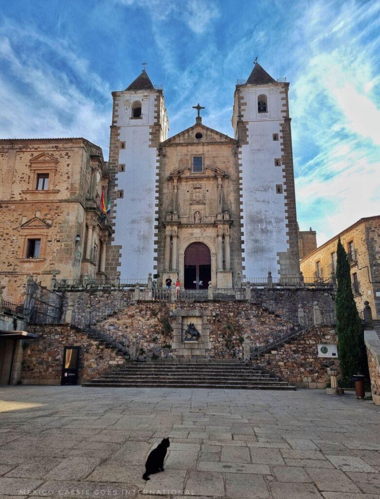 church with two white towers, one on either side. black cat sitting on terrace in front at bottom of stairs