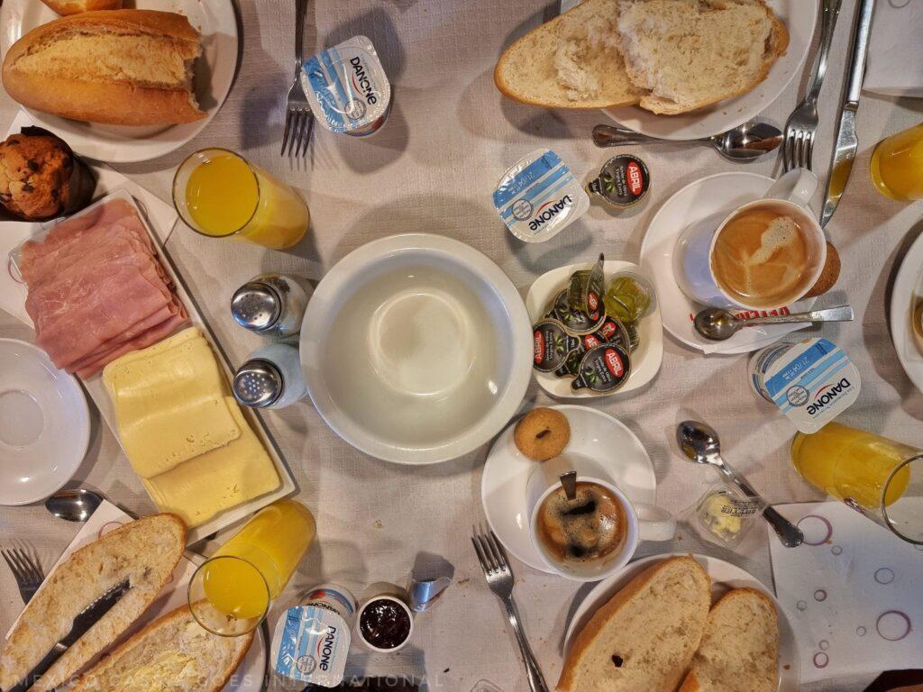 breakfast table with plate of ham and cheese, breads, yoghurts