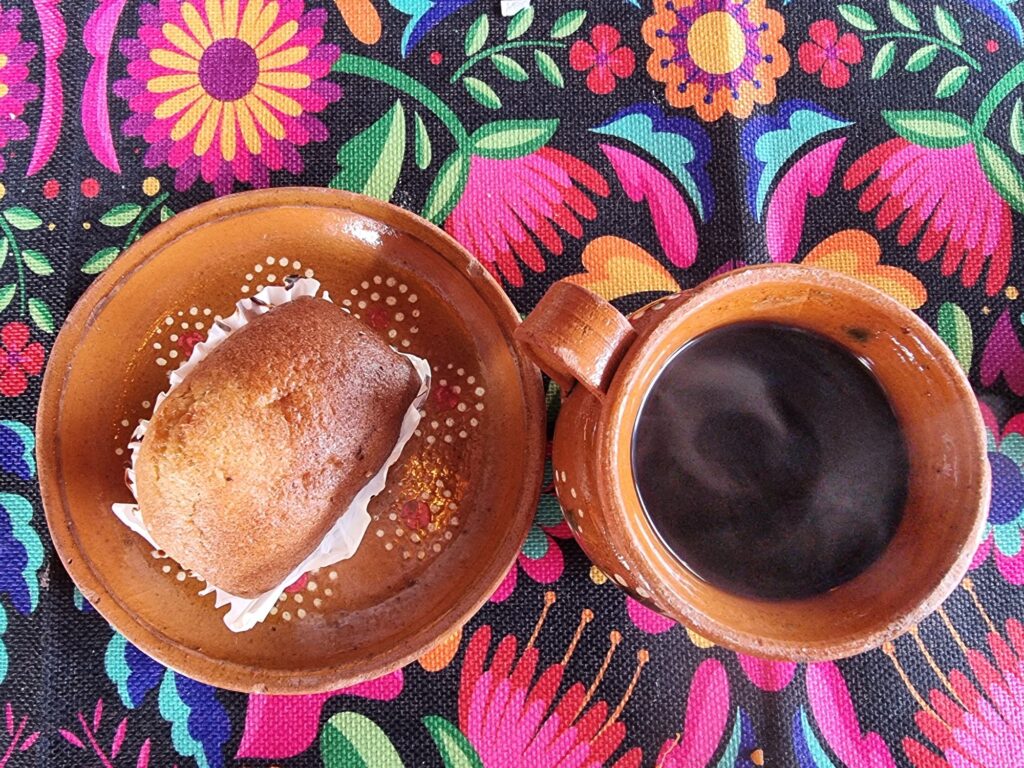 black coffee and pastry on plate- colourful Mexican table cloth underneath