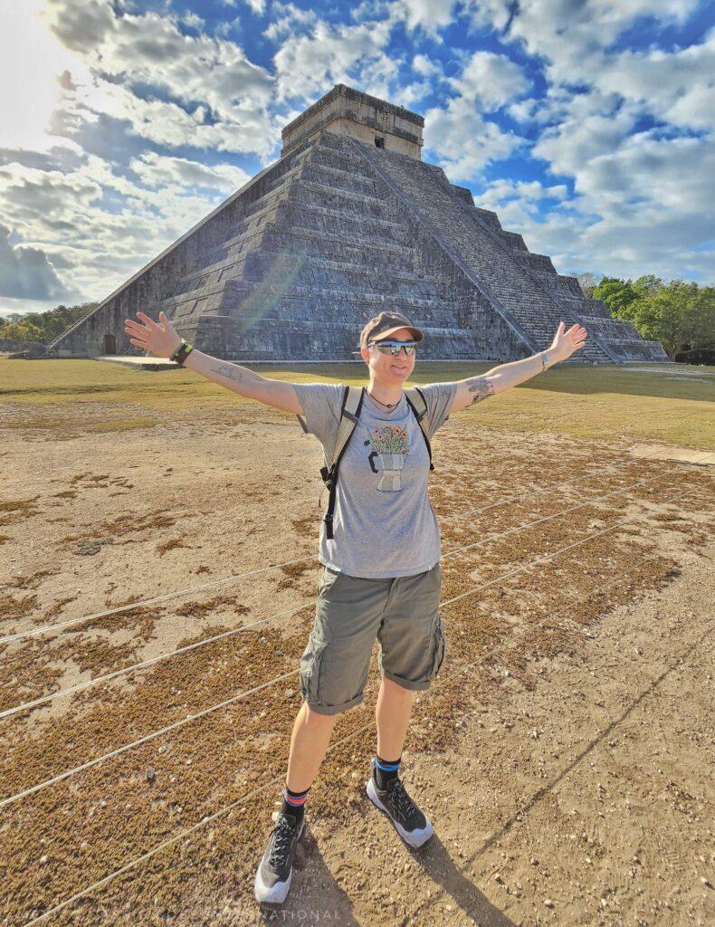 Cass standing in front of a pyramid with arms outstretched
