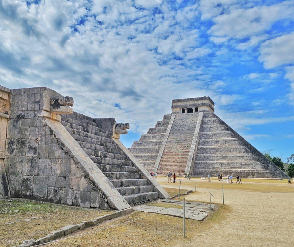 chichen itza pyramid and one other shorter building in front, very few people, blue sky with clouds