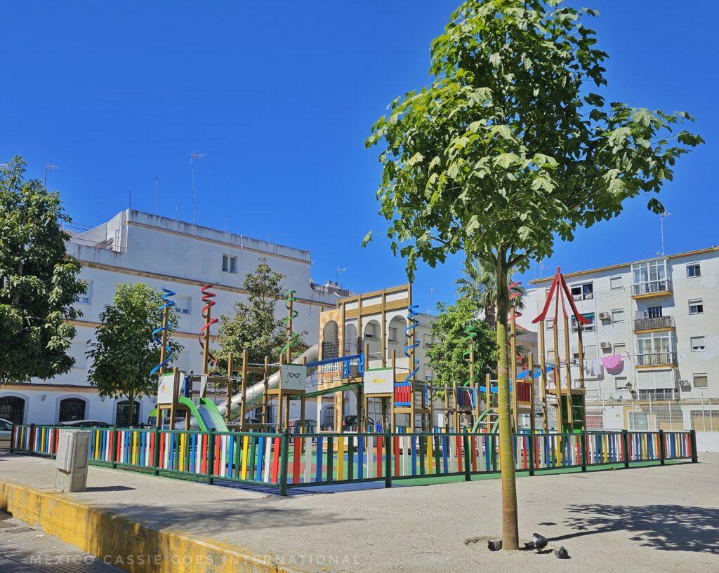 playground in a plaza surrounded by white buildings and trees
