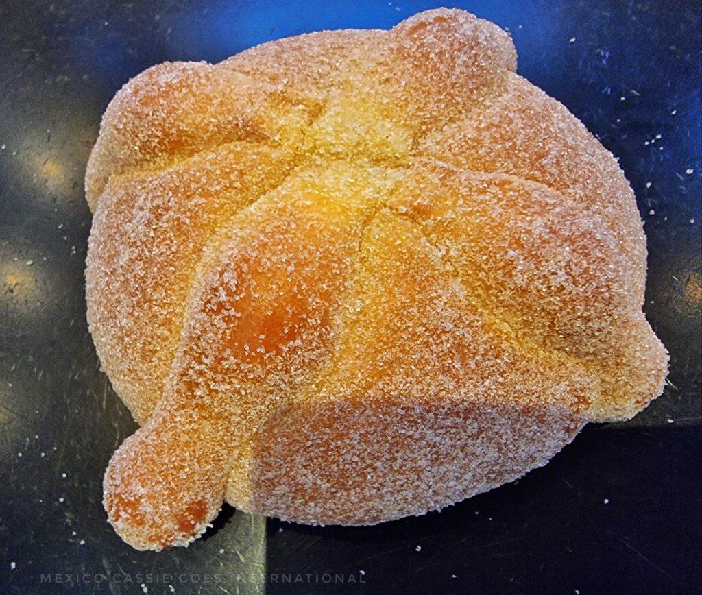 close up of a pan de muerto - sweet bread covered in sugar with 4 extra pieces of dough on top in shape of bones