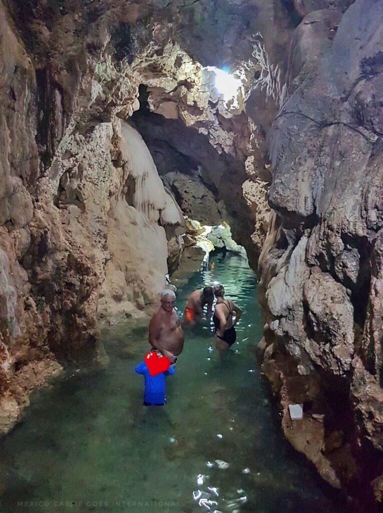 3 adults and a kid in a cave pool. kid has face blurred out with a pixel heart