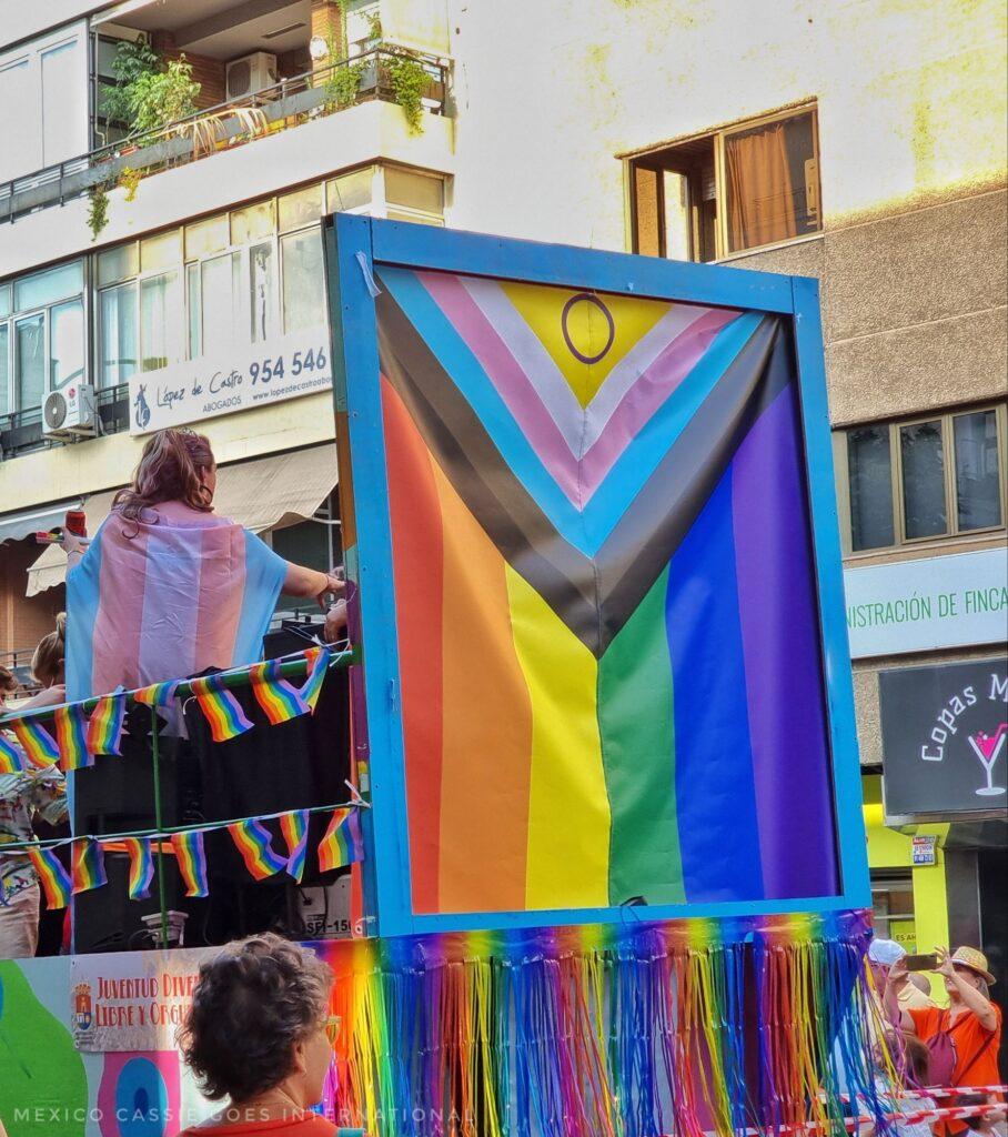 inclusive LGBTQIA+ flag on back of float in pride parade, can see one person in trans flag on bus