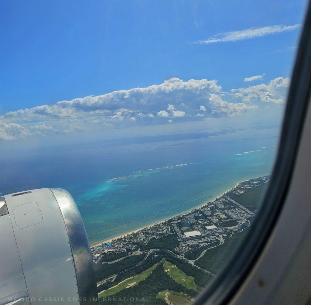 view out of an aeroplane window, can just see engine, coast and sea below