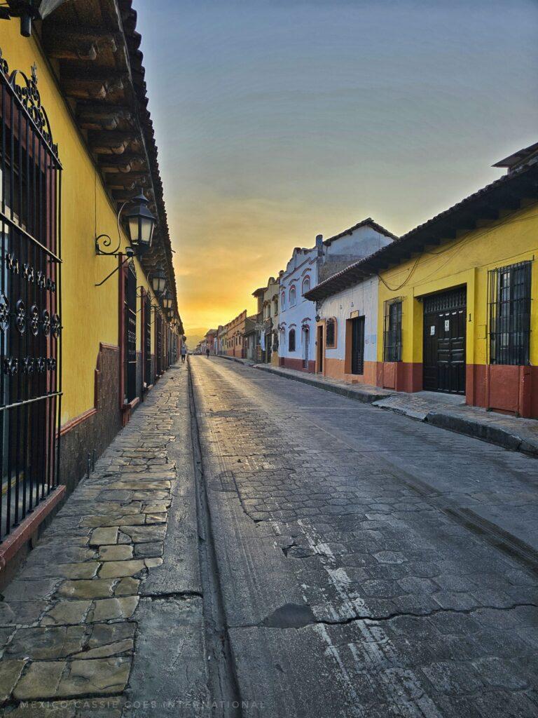 empty street with colourful buildings on either side, sun setting in distance