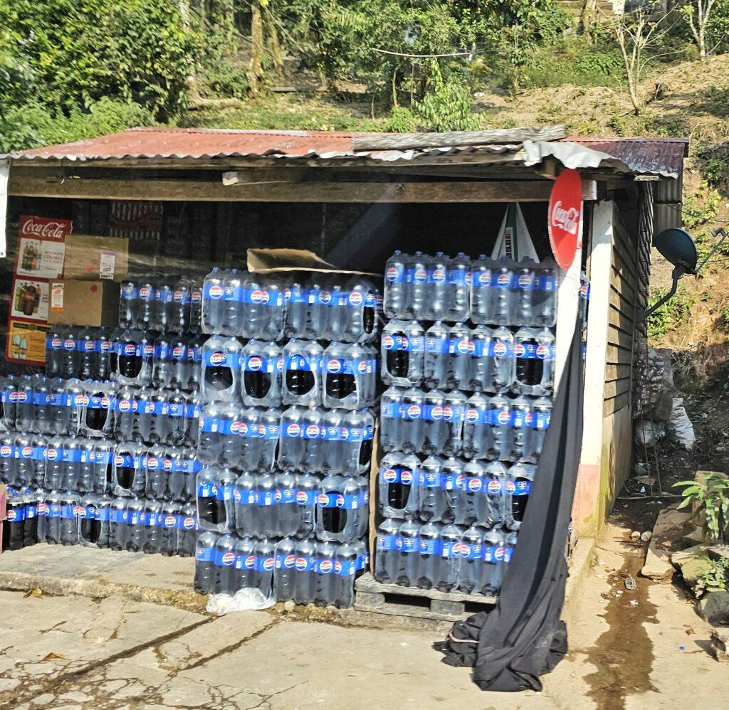 bottles of pepsi stored in a makeshift shelter, coke sign above