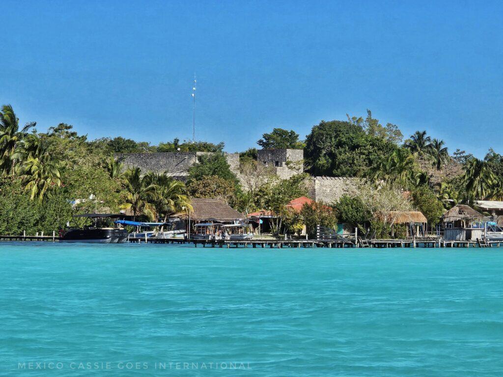 gorgeous turquoise water, thatched buildings on land, trees, blue sky