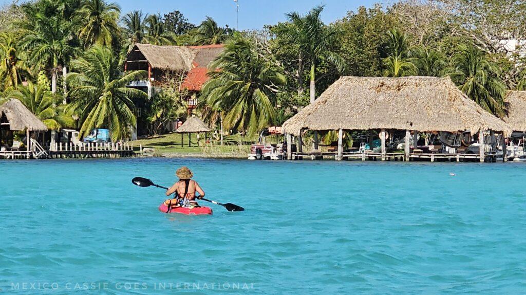 turquoise water, person in red kayak, thatched buildings and palms on shore