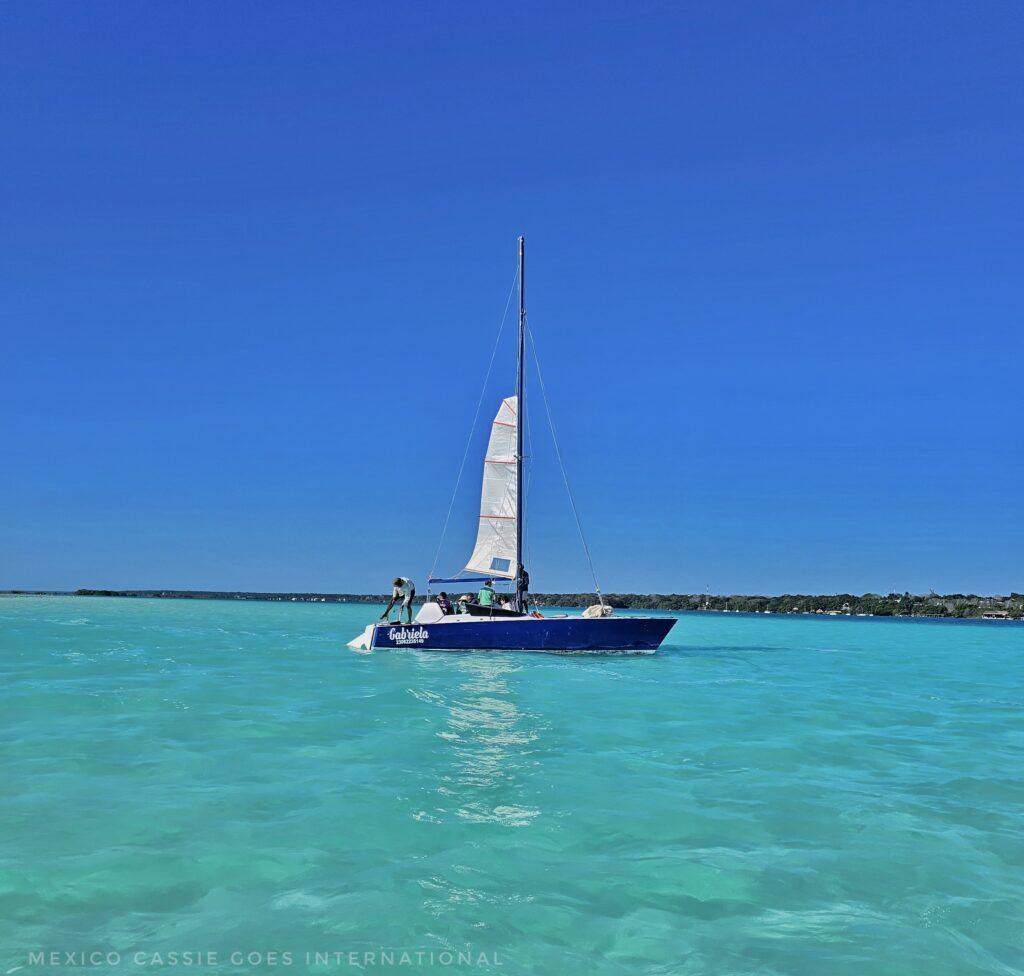 sailing boat with small white sail on turquoise water, perfect blue sky