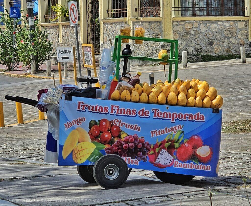 mango cart - top is full of mangos, sign advertising fruits on side