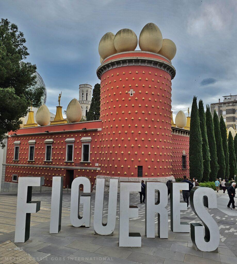 Figueres letters in white in front of Dalí castle  red with tower and gold eggs on top