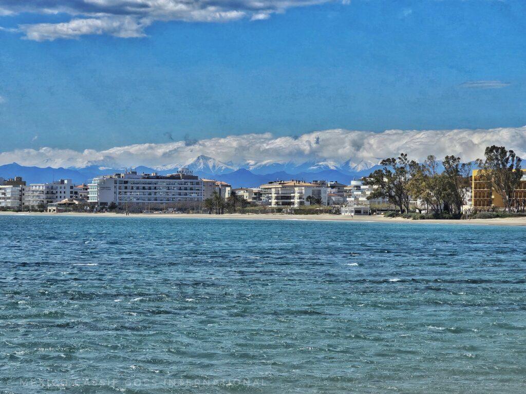 ocean, beach, buildings, snowy mountains in far distance