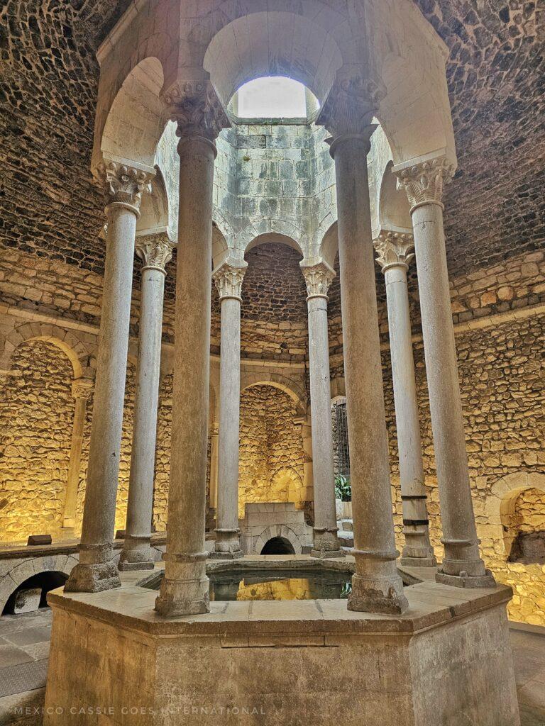 inside of the arab baths, white marble columns around a small pool of water, stretching up to ceiling