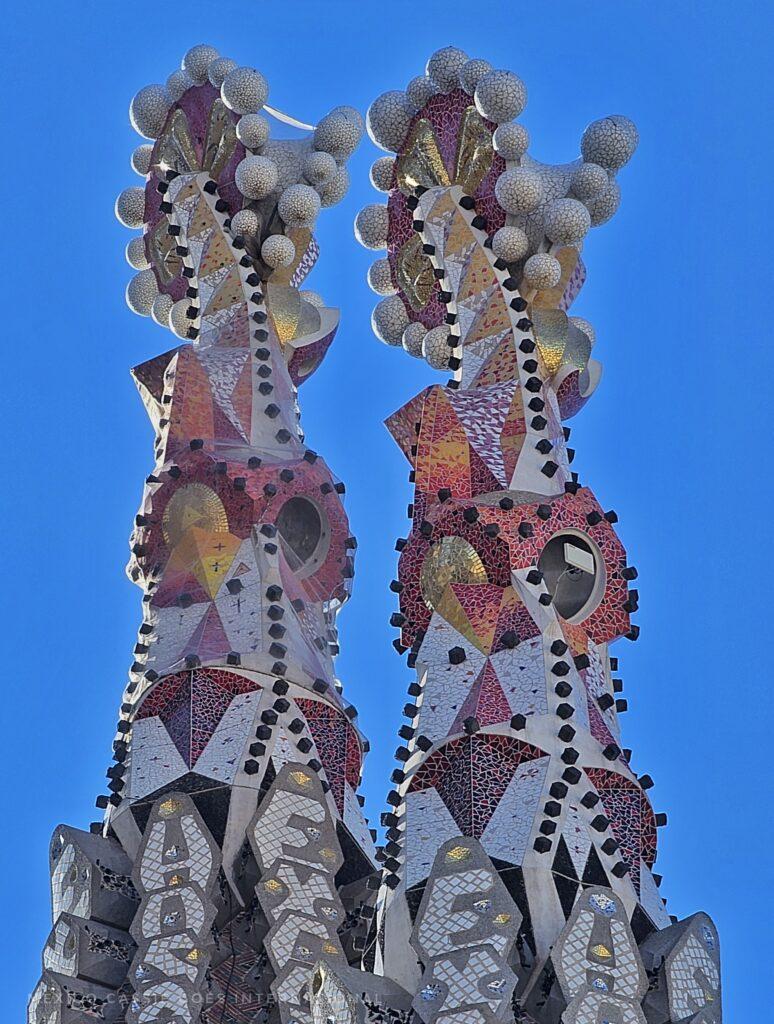 two towers from the Sagrada Familia -white with coloured sections, top of both with multiple balls attached