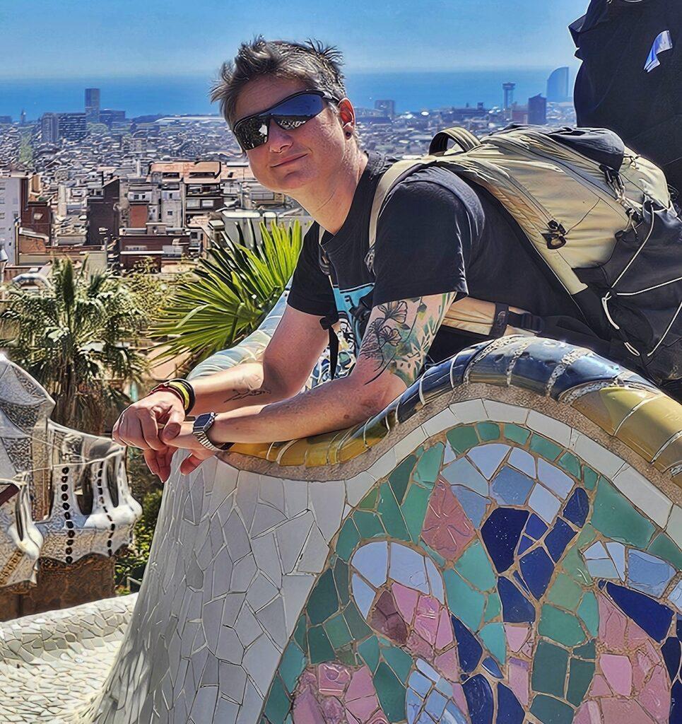 Cass posing in Park Güell - leaning arms on low wall, bag on back, view of Barcelona in distance