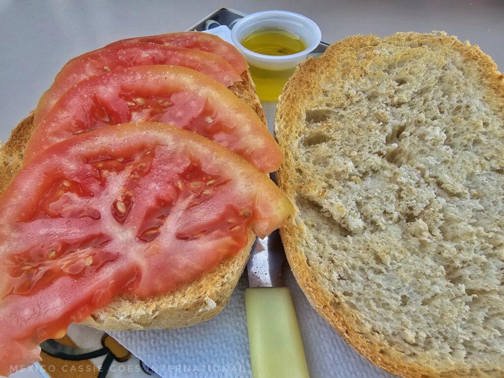two slices of bread, one with sliced tomato, small cup of oil