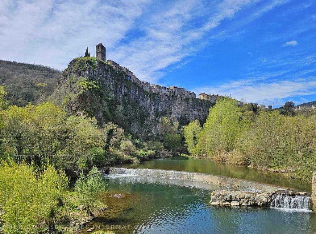 river, small waterfall, basalt cliff above with town perched on it