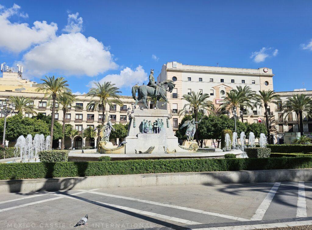 large open plaza, fountain with typical man on horse statue, buildings and palm trees