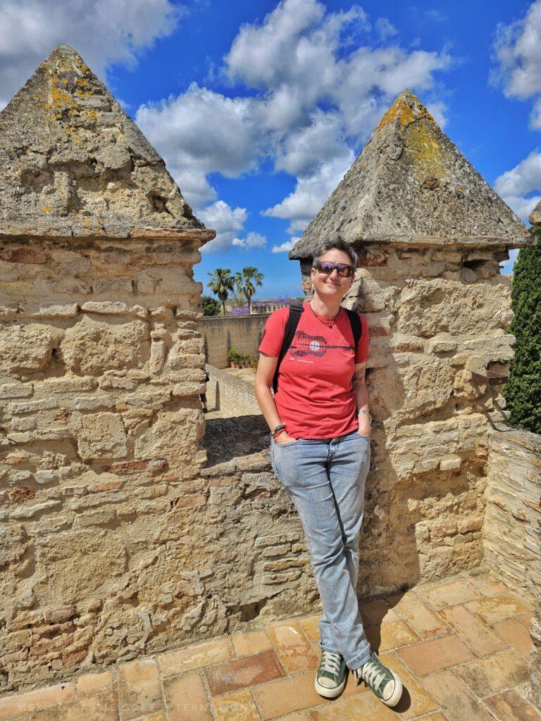 Cass in jeans and red tshirt leaning against wall of the alcazar