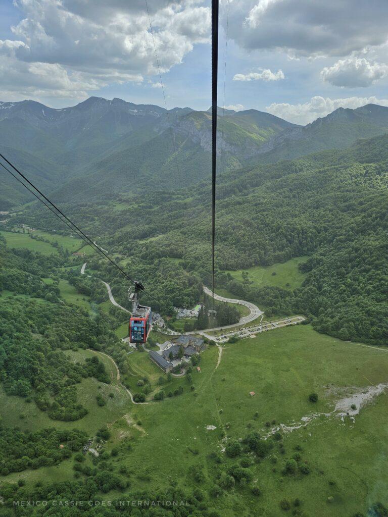 looking down from top of a cable car point over green fields, cable car cables visible