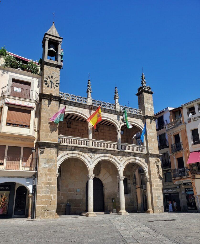 town hall building, tall clock tower on one side, four flags flying (blue sky)