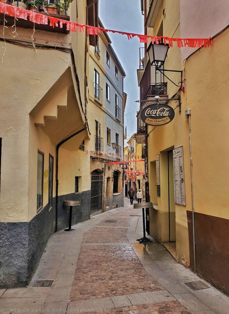 photo of narrow street in old spanish town, red bunting between houses at front