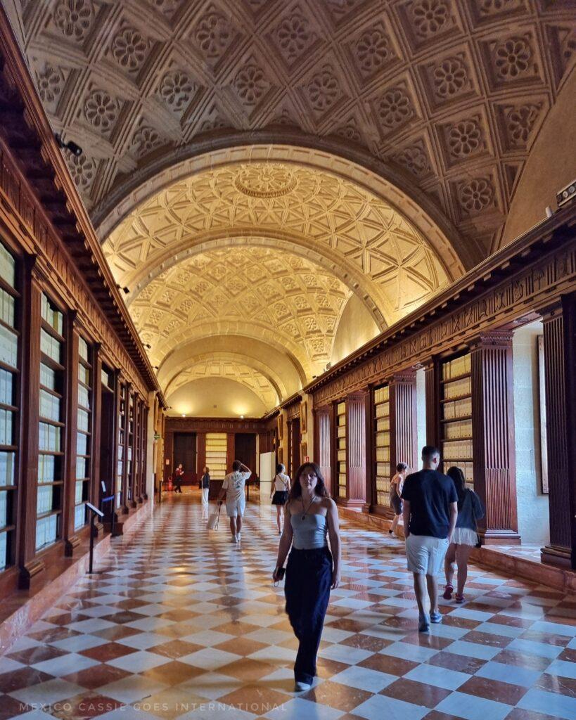 interior of archivo de indias, red and white tiled floor, wooden cabinets filled with files linking walls, arched ceiling, people walking