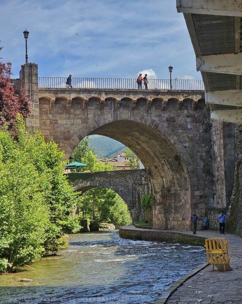 small river from running under tall medieval bridge, people on bridge