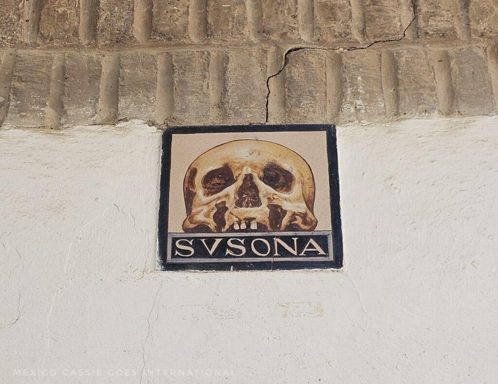 wall with a single tile on it that says SVSONA and has a skull above the writing