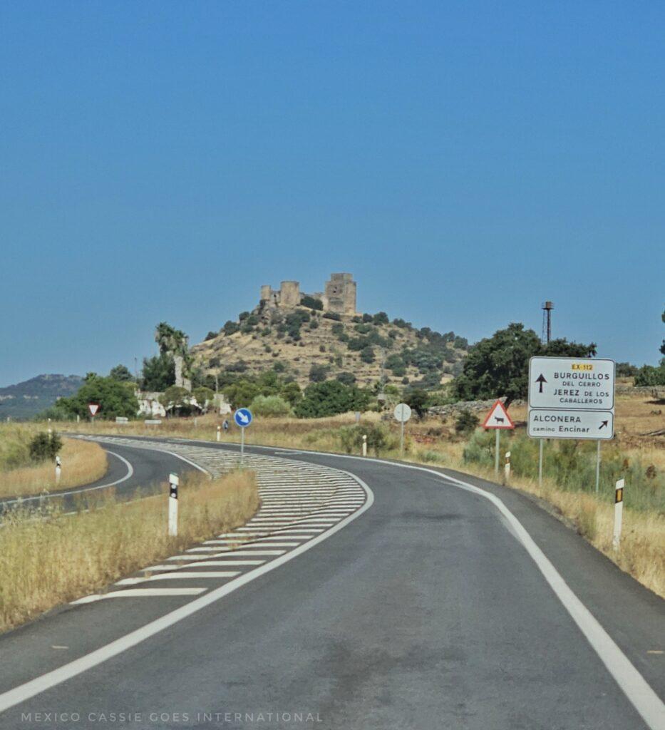 empty road with castle on hill in distance, road signs nearby